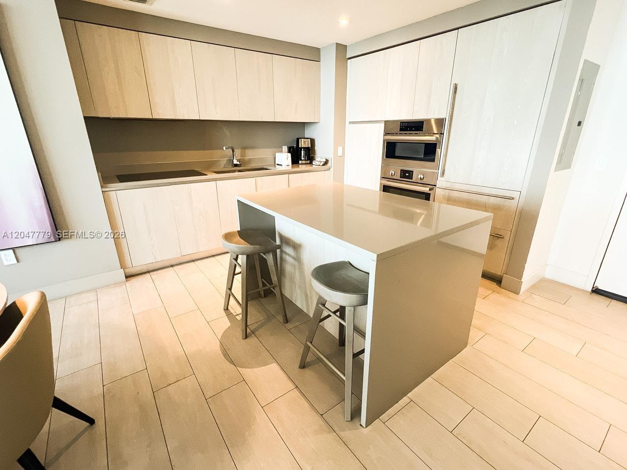 A modern kitchen features light wood cabinetry, a gray island with two stools, and stainless appliances — 4010 S Ocean Dr # T3505, Hollywood FL 33019, HOLLYWOOD, FL