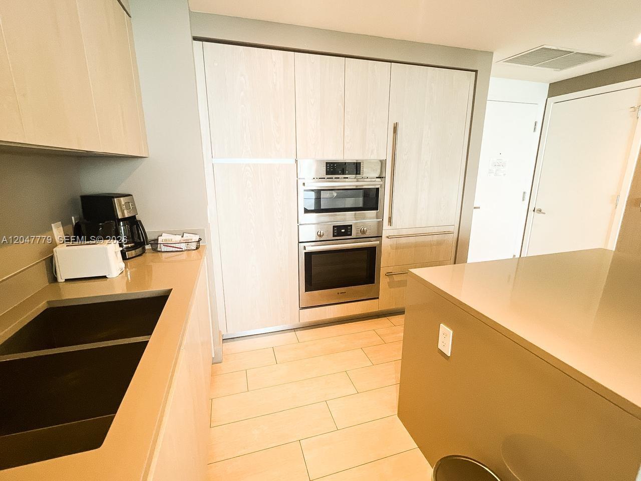A modern kitchen features light wood cabinetry, stainless steel appliances, and light-colored tile flooring — 4010 S Ocean Dr # T3505, Hollywood FL 33019, HOLLYWOOD, FL