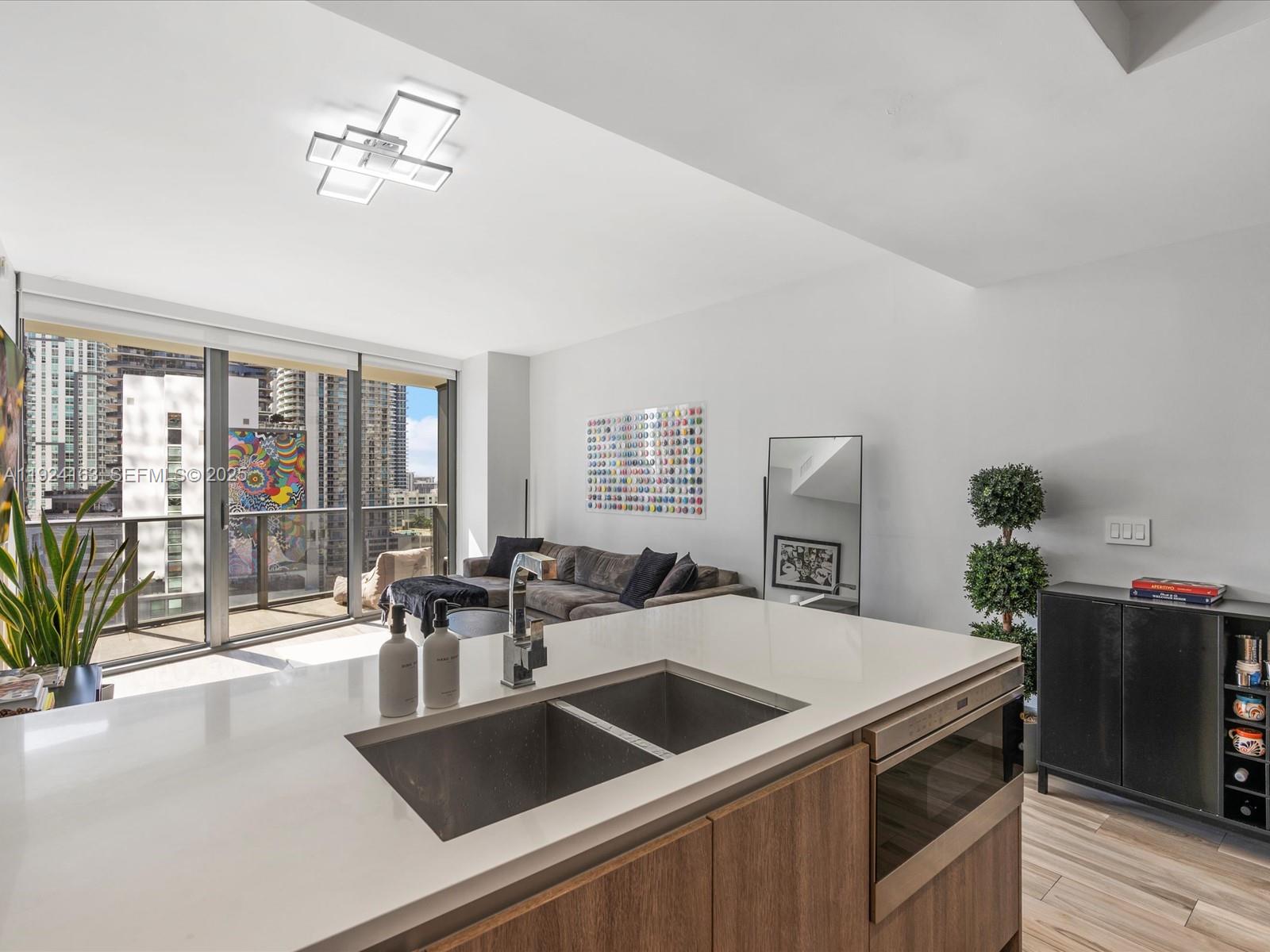 A modern kitchen island with a stainless steel sink overlooks a living area and balcony — 801 S Miami Ave # 1603, Miami FL 33130, MIAMI, FL