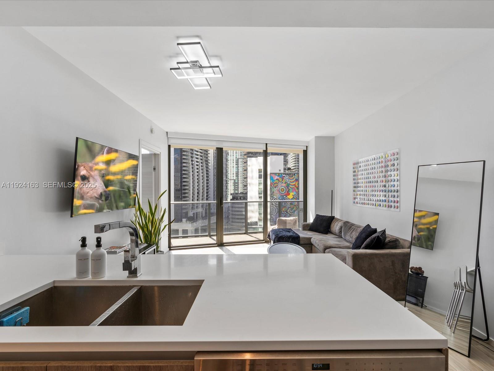 A modern kitchen island overlooks a living room with a sofa, balcony, and city views — 801 S Miami Ave # 1603, Miami FL 33130, MIAMI, FL