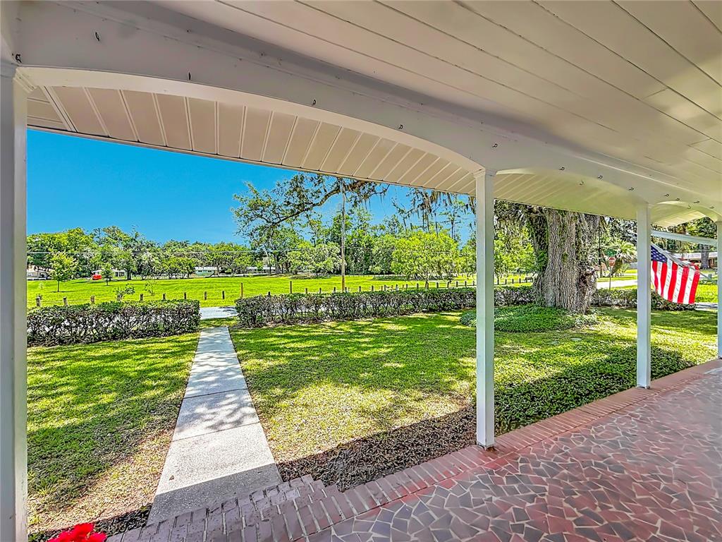 A covered brick porch overlooks a grassy yard with a sidewalk and mature trees — 848 SE 23RD STREET, OCALA, FL