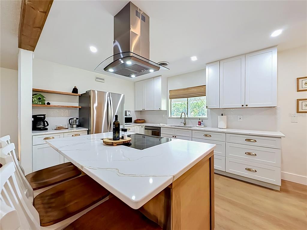 A kitchen features white cabinets, a marble-topped island with a cooktop, and stainless steel appliances — 848 SE 23RD STREET, OCALA, FL