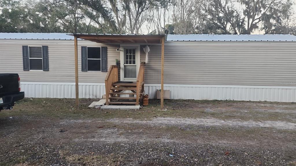A single-story mobile home with tan siding, a metal roof, and a wooden front porch — 1333 WILKINSON DRIVE, PLANT CITY, FL