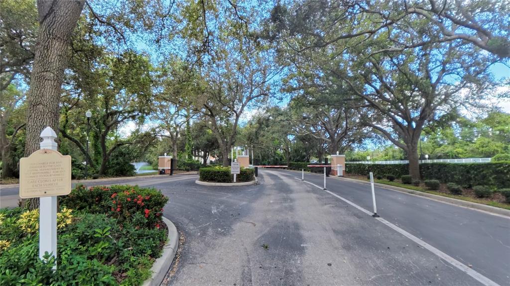 A gated entrance with a paved driveway, lush trees, and a small sign on the left — 4134 CENTRAL SARASOTA PKWY UNIT 1722, SARASOTA, FL