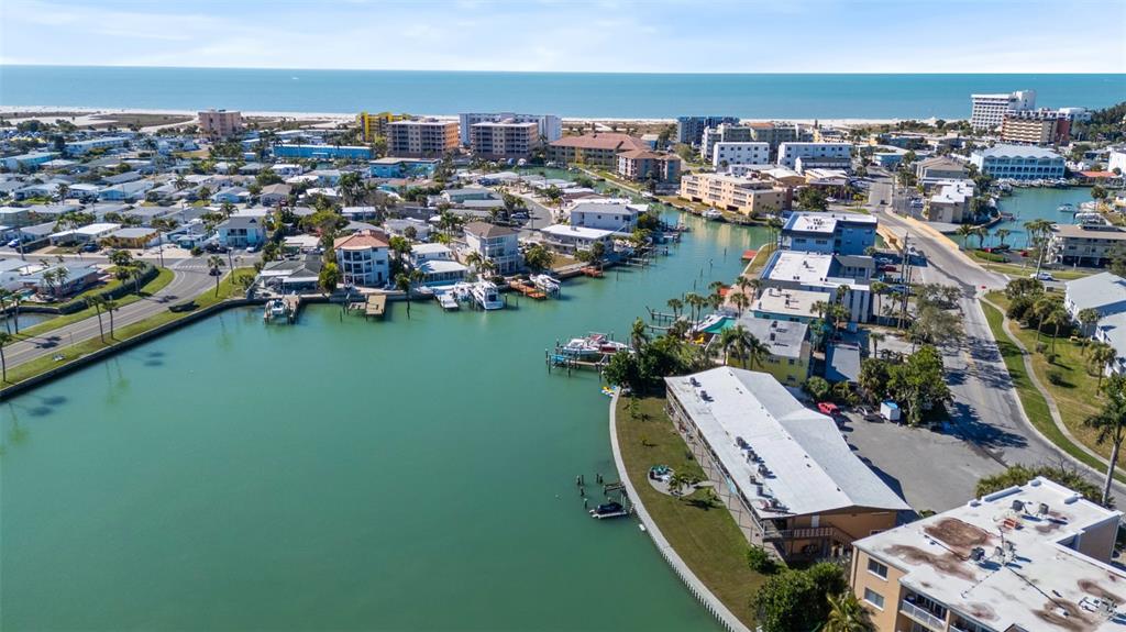 An aerial view shows a coastal waterway surrounded by residential buildings, docks, and boats — 275 116TH AVENUE, TREASURE ISLAND, FL