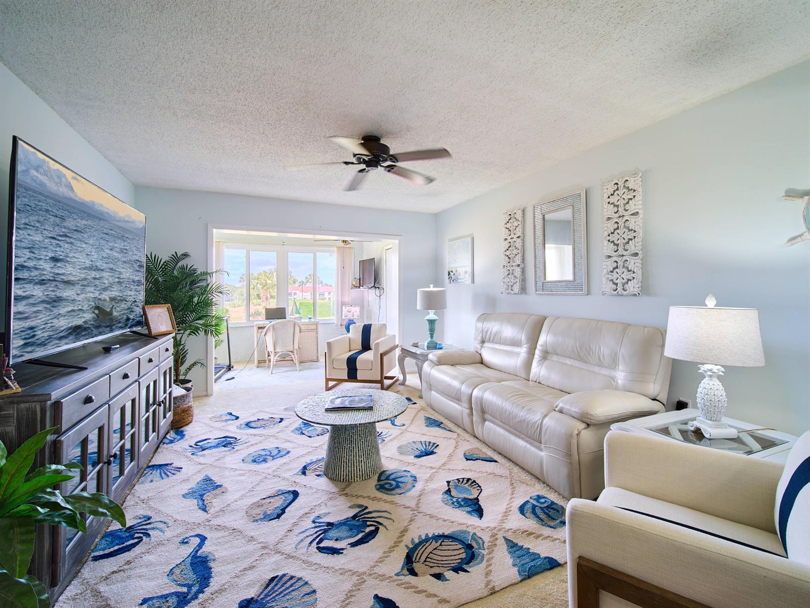 A living room features a white leather sofa, a coastal-themed area rug, and a television — 5363 SE Miles Grant Road # D202, Stuart FL 34997, STUART, FL