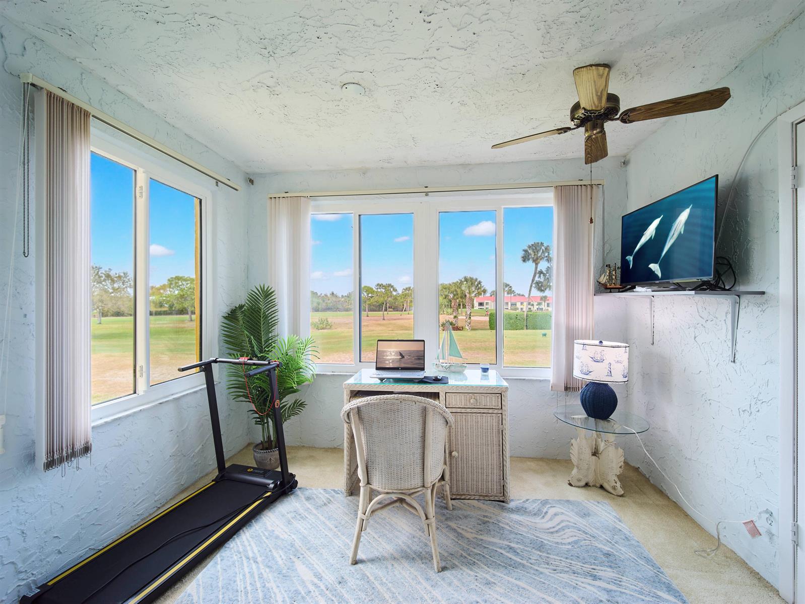A sunroom features a treadmill, a wicker desk with a laptop, and views of a golf course — 5363 SE Miles Grant Road # D202, Stuart FL 34997, STUART, FL