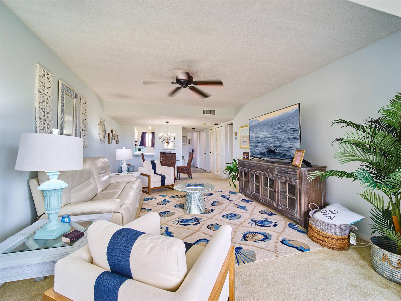 A living room features a beige sofa, two armchairs, a television, and a coastal-themed rug — 5363 SE Miles Grant Road # D202, Stuart FL 34997, STUART, FL