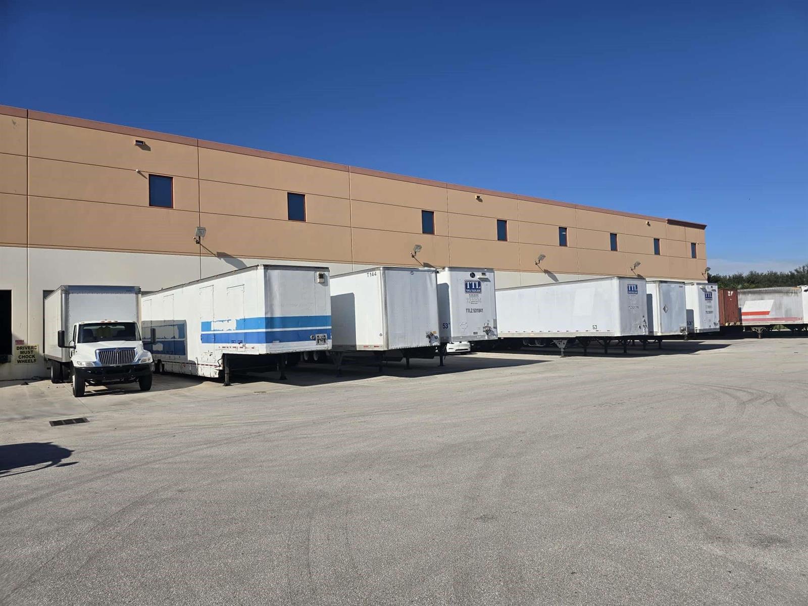 A row of semi-trailers is parked at a loading dock against a tan industrial building — 9608-9616 Premier Parkway, Miramar FL 33025, MIRAMAR, FL