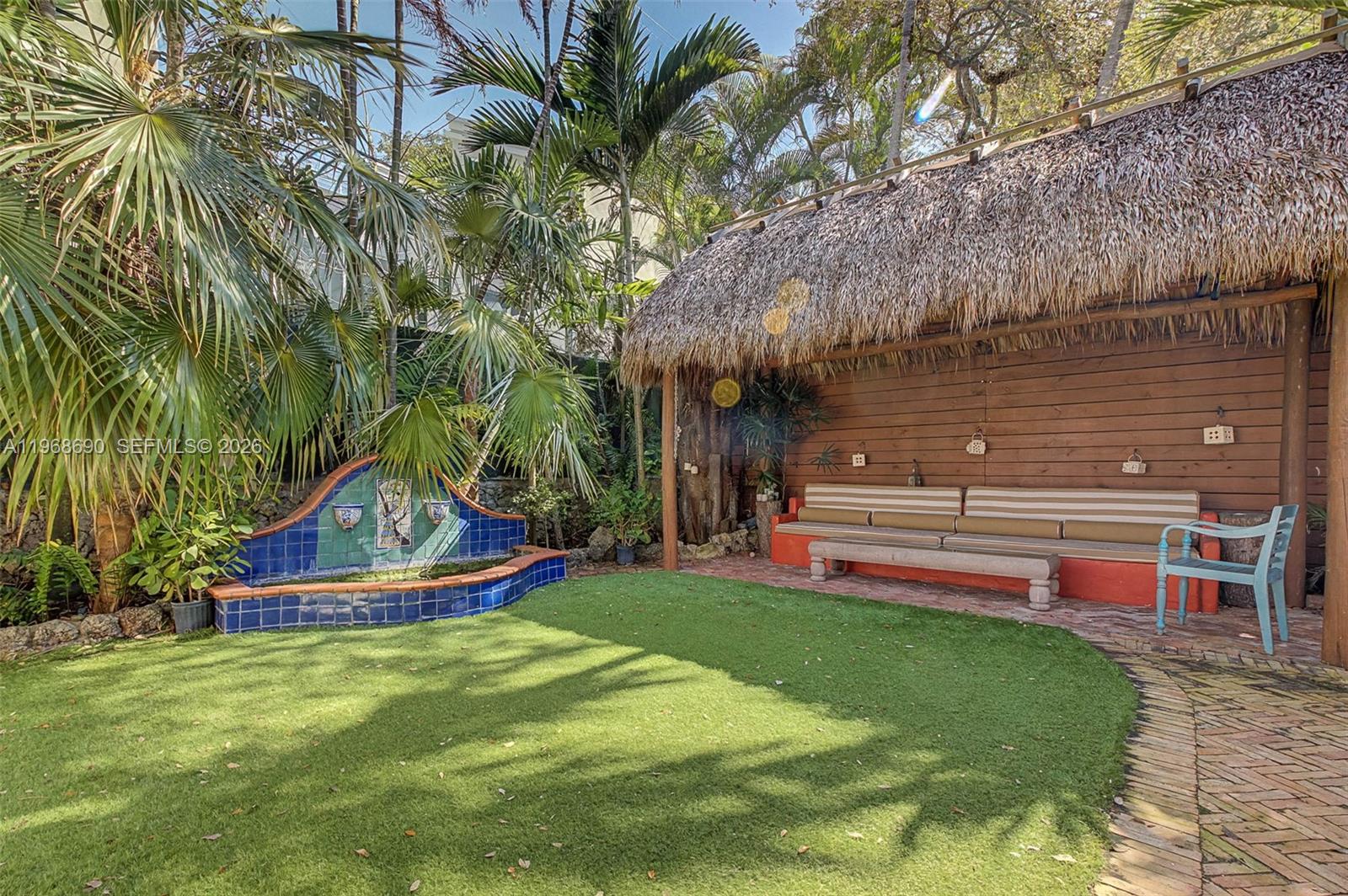 A backyard features a thatched-roof tiki hut with built-in seating, a blue-tiled fountain, and palms — 3233 Crystal Ct, Miami FL 33133, MIAMI, FL
