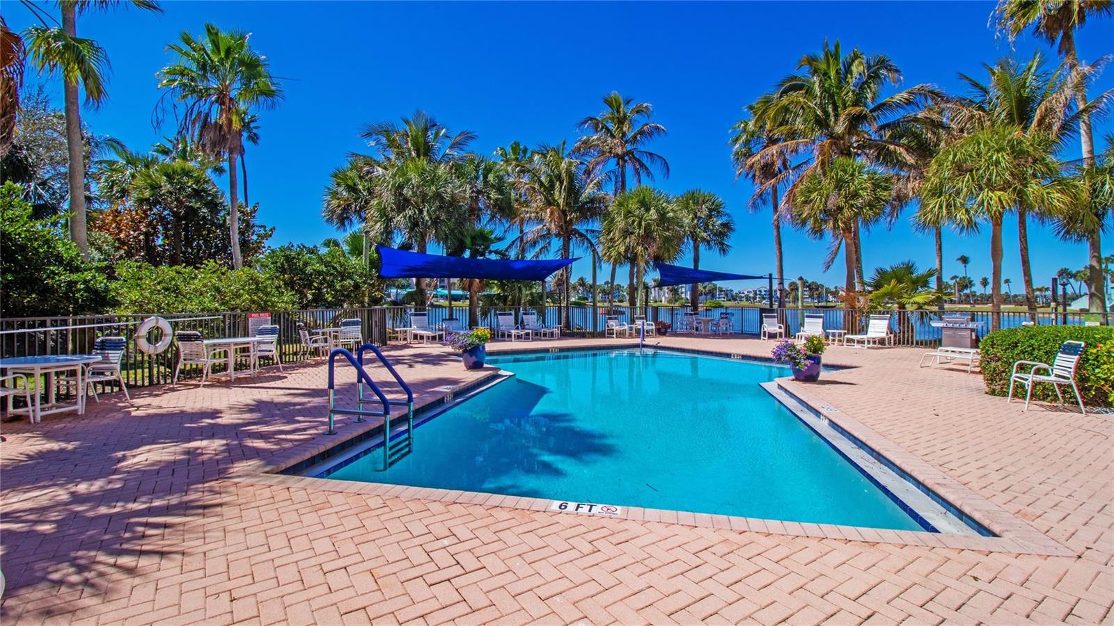 A rectangular swimming pool is surrounded by a brick patio, palm trees, and lounge chairs — 221 NE Plantation Road # 213, Stuart FL 34996, STUART, FL