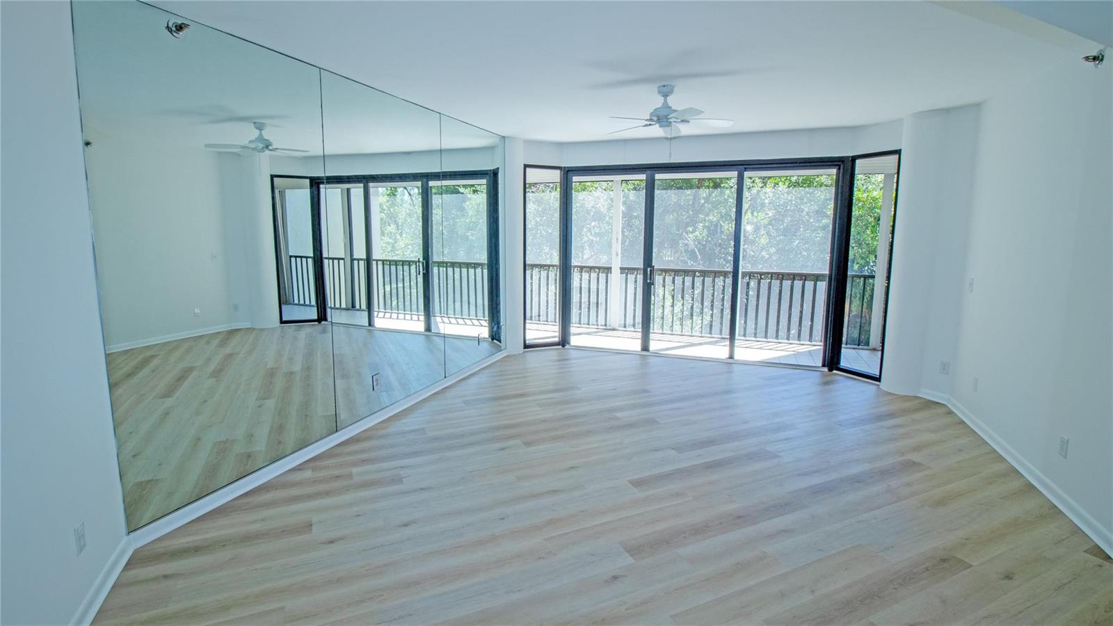 An empty room with light wood-look flooring, a large mirrored wall, and sliding glass doors — 221 NE Plantation Road # 213, Stuart FL 34996, STUART, FL