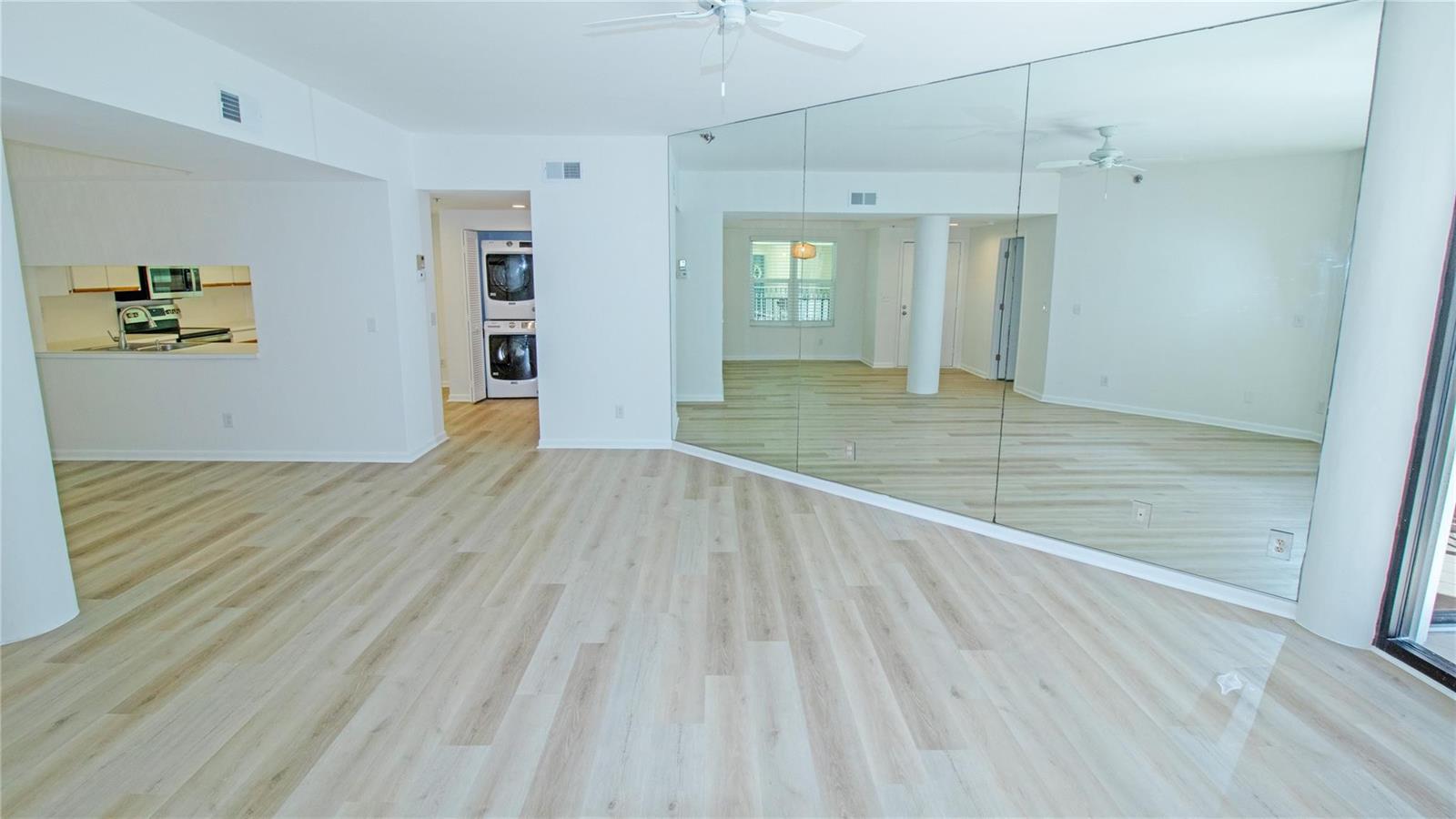 An open living area features light wood-look flooring, a mirrored wall, and a laundry closet — 221 NE Plantation Road # 213, Stuart FL 34996, STUART, FL