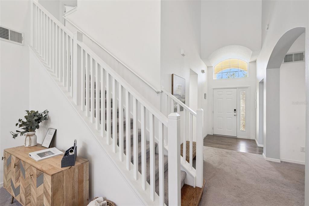 A bright entryway features a white staircase, carpeted flooring, and a front door with sidelights — 4661 GOLDEN BEACH COURT, KISSIMMEE, FL