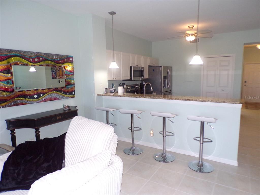 A kitchen with a breakfast bar, white cabinets, and stainless steel appliances overlooks a living area — 3500 MONDOVI COURT UNIT 811, PUNTA GORDA, FL