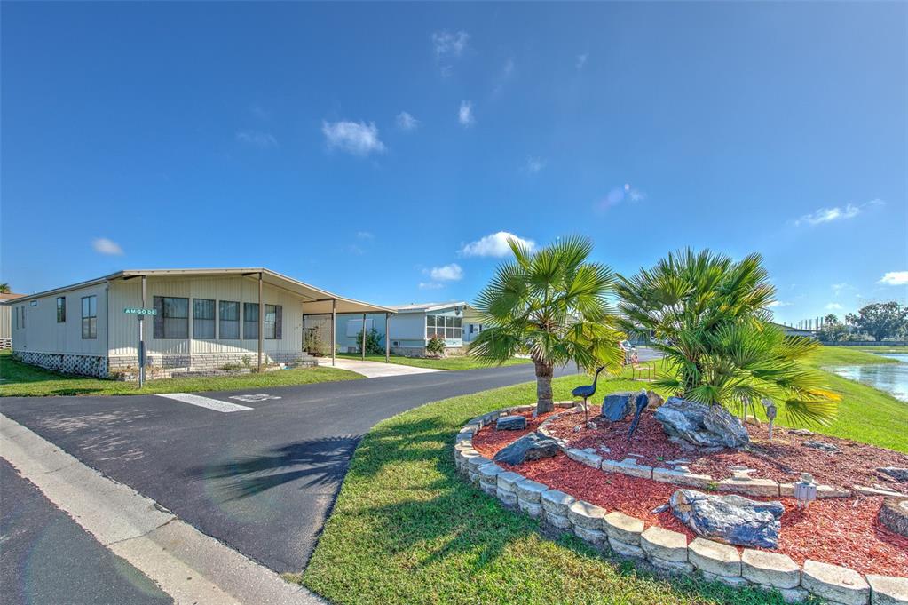 A mobile home with a carport sits next to a landscaped palm tree garden — 37605 AMIGO DRIVE, ZEPHYRHILLS, FL