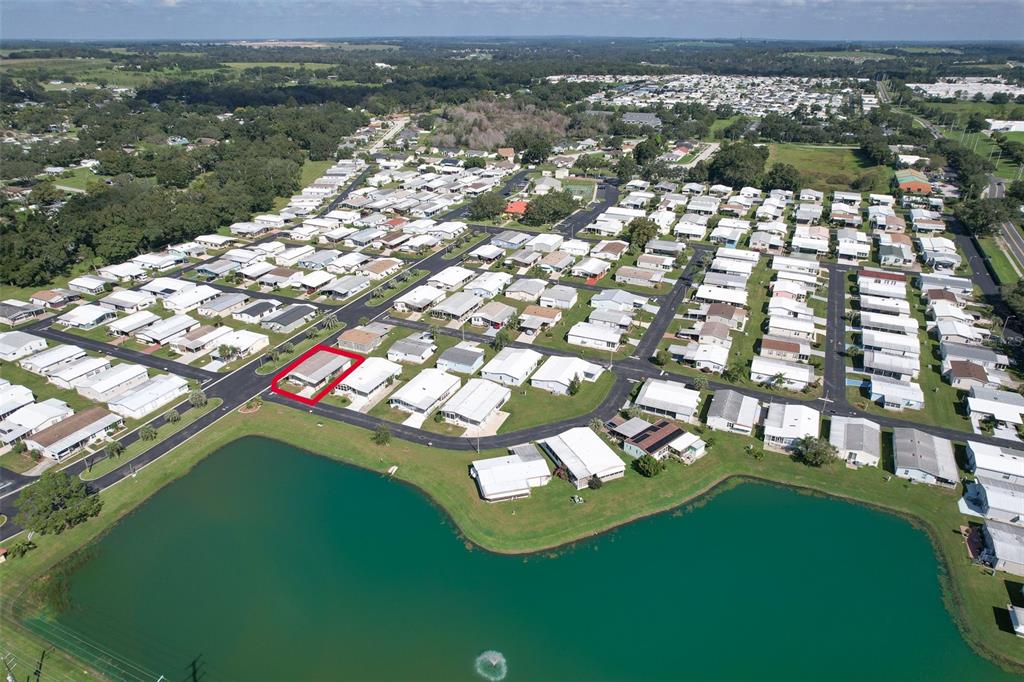 An aerial view shows a mobile home community with a highlighted house near a lake — 37605 AMIGO DRIVE, ZEPHYRHILLS, FL