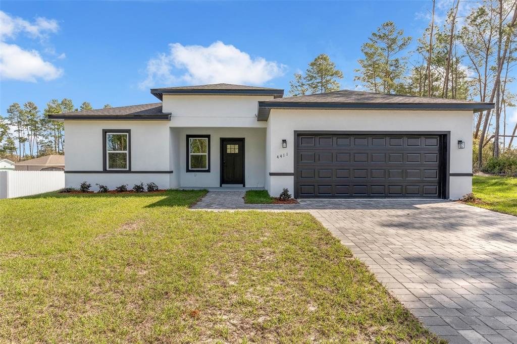 A single-story house with white stucco walls, a dark garage door, and a paved driveway — 4411 SW 172ND STREET ROAD, OCALA, FL