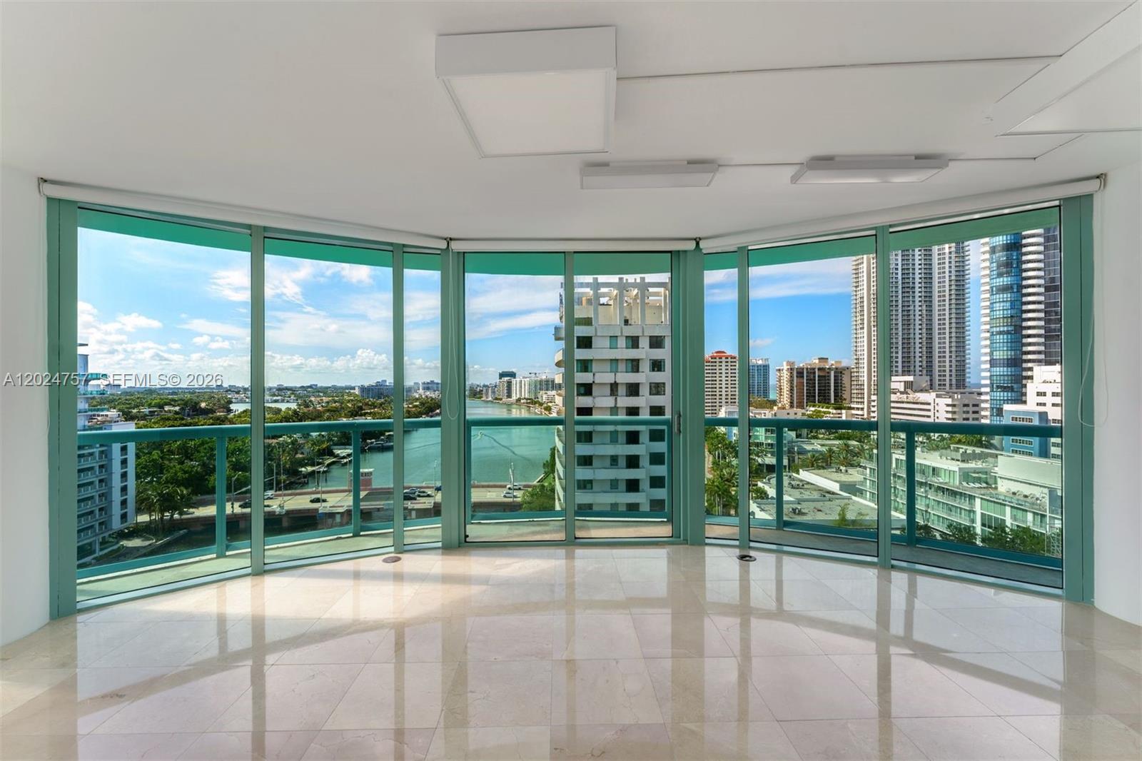 An empty room with light-colored tile floors features floor-to-ceiling windows overlooking a city waterway — 6000 Indian Creek Dr # 14B, Miami Beach FL 33140, MIAMI BEACH, FL