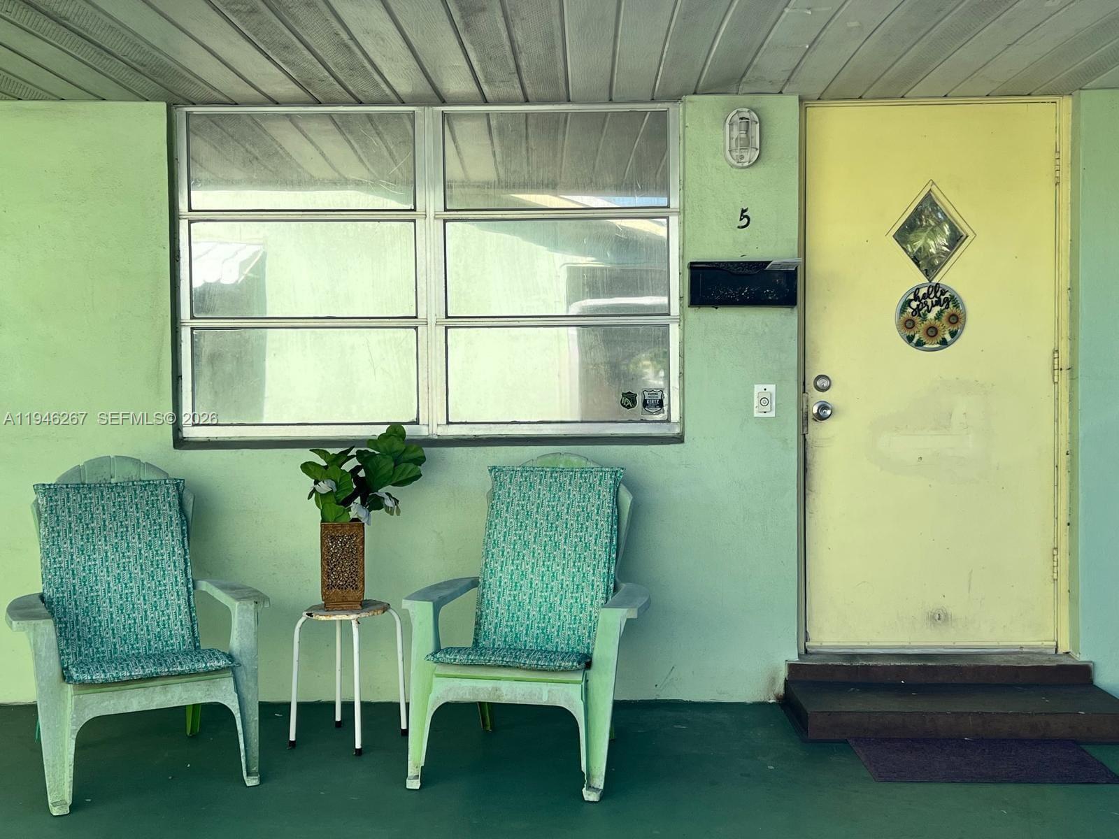 A light green exterior wall features a yellow door, a large window, and two chairs — 2702 Pierce St # 5, Hollywood FL 33020, HOLLYWOOD, FL