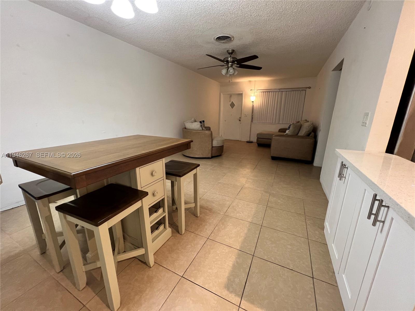A kitchen island with stools sits in an open-concept living area with tiled floors — 2702 Pierce St # 5, Hollywood FL 33020, HOLLYWOOD, FL