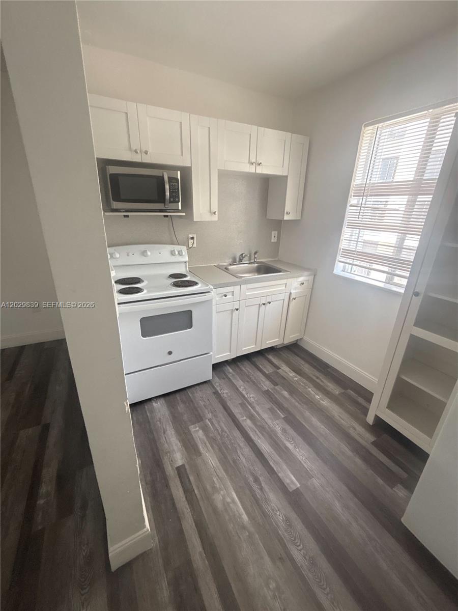 A small kitchen features white cabinets, a white stove, a microwave, and wood-look flooring — 542 NW 8th St # 11, Miami FL 33136, MIAMI, FL