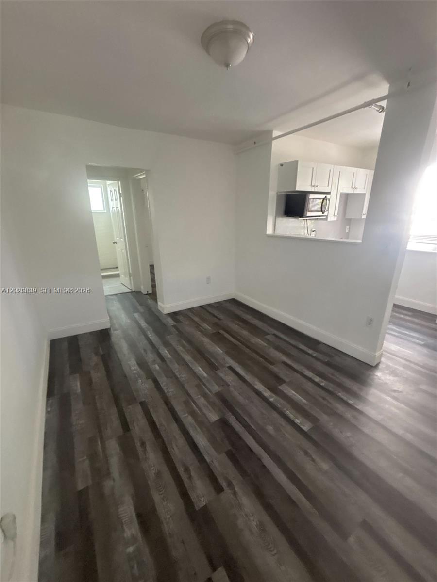 An interior room features dark wood-look flooring, white walls, and a kitchen pass-through window — 542 NW 8th St # 11, Miami FL 33136, MIAMI, FL