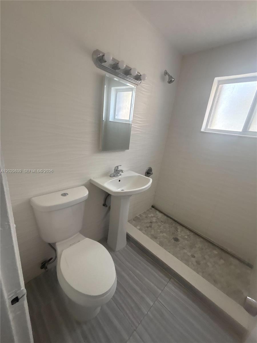A bathroom features a pedestal sink, a toilet, and a walk-in shower with stone flooring — 542 NW 8th St # 11, Miami FL 33136, MIAMI, FL
