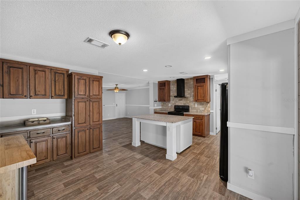 A kitchen features wood cabinets, a stone backsplash, a center island, and wood-look flooring — 4830 NE 121 AVENUE, WILLISTON, FL