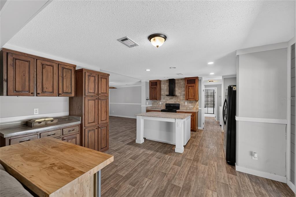A kitchen features wood cabinets, a white island, stone backsplash, and wood-look flooring — 4830 NE 121 AVENUE, WILLISTON, FL