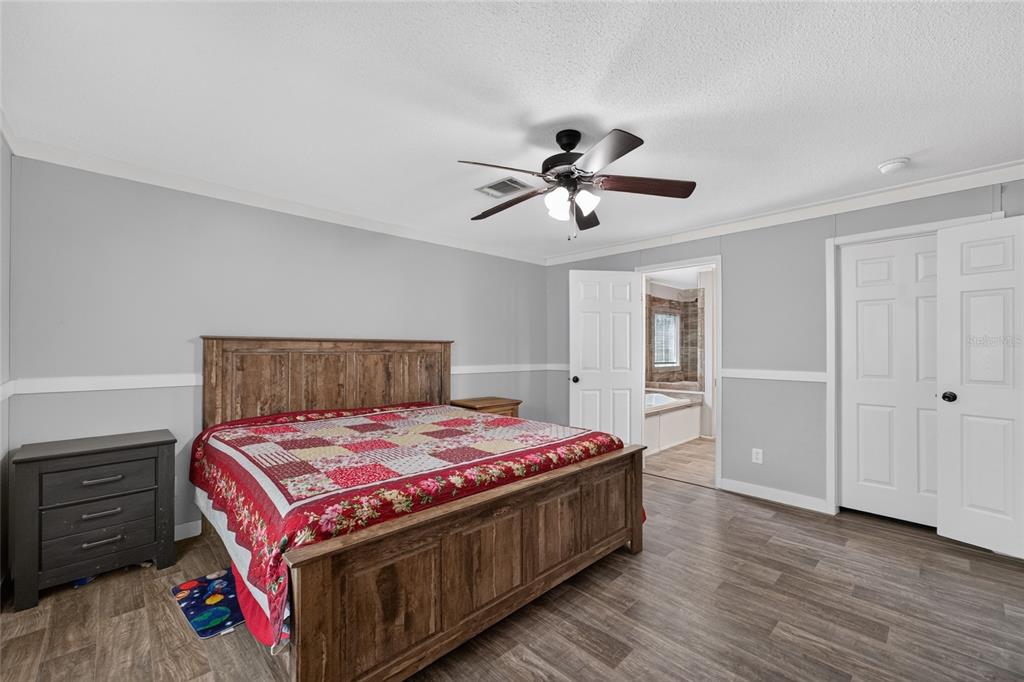 A bedroom features a wooden bed frame, gray walls, wood-look flooring, and an attached bathroom — 4830 NE 121 AVENUE, WILLISTON, FL