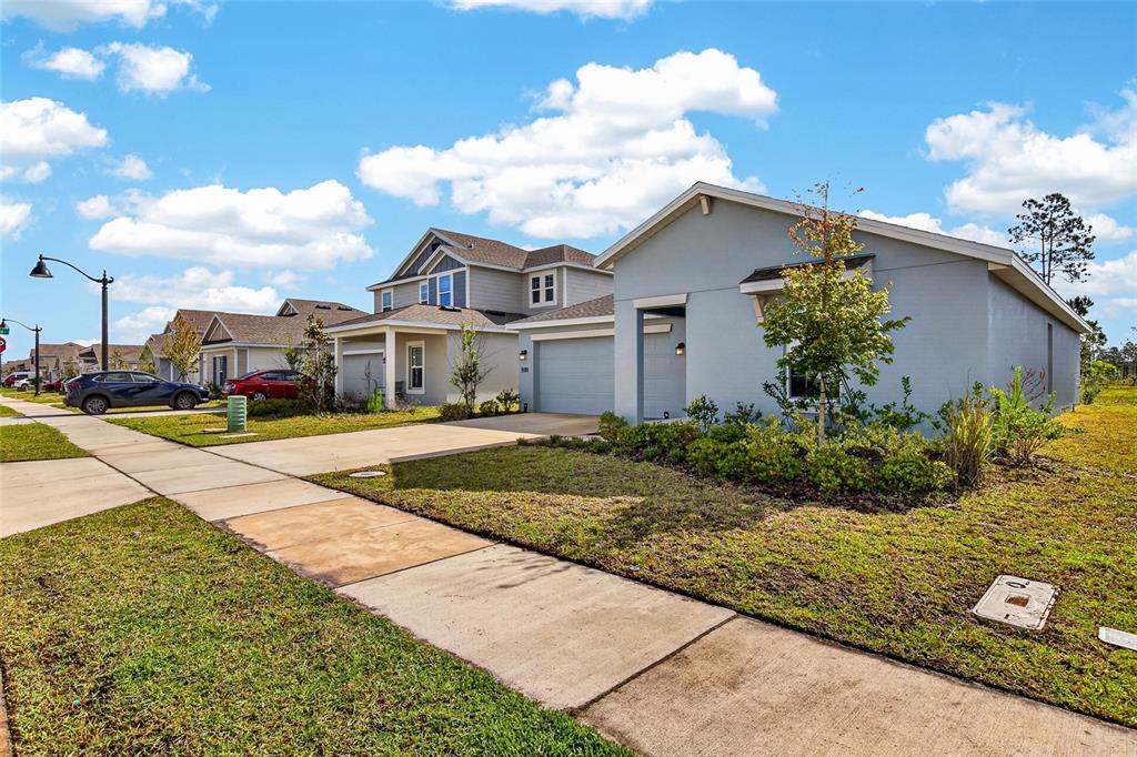 A street view shows several suburban houses with driveways, lawns, and sidewalks under a blue sky — 2212 GREEN VALLEY STREET, DAYTONA BEACH, FL