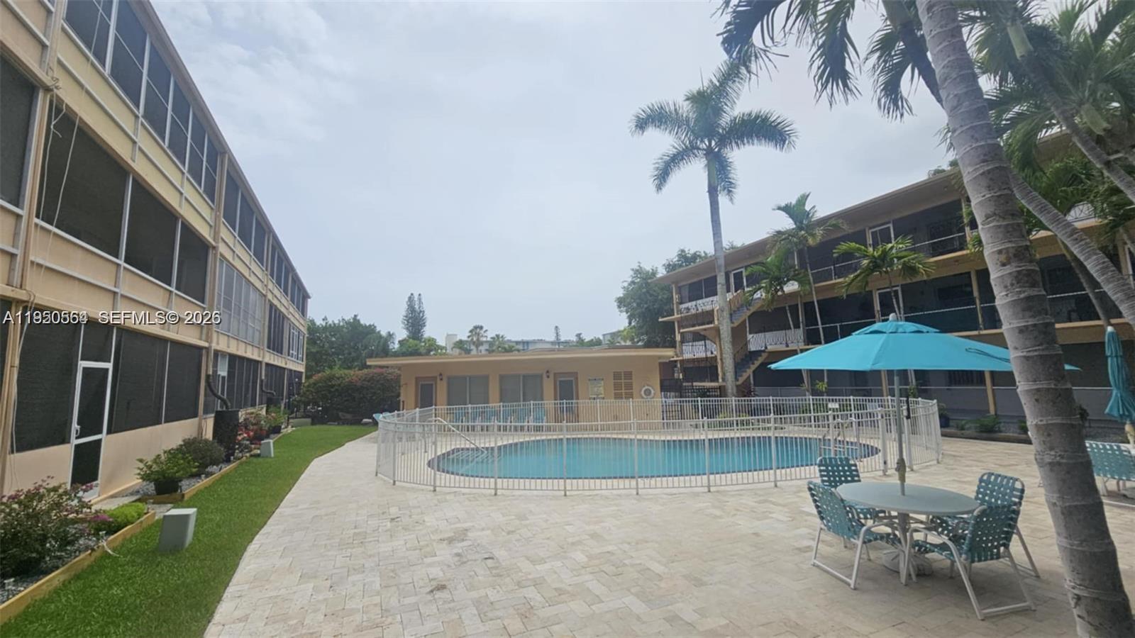 An outdoor swimming pool is surrounded by a white fence, patio furniture, and apartment buildings — 1500 NE 127th St # 103, North Miami FL 33161, NORTH MIAMI, FL