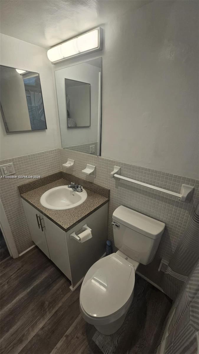 A small bathroom features a vanity with a speckled countertop, toilet, and tiled walls — 1500 NE 127th St # 103, North Miami FL 33161, NORTH MIAMI, FL