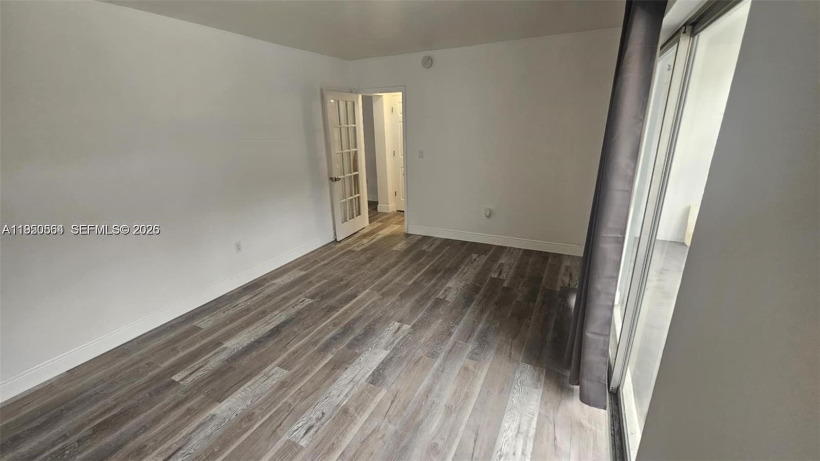 An empty room features white walls, wood-look flooring, and a glass-paned door — 1500 NE 127th St # 103, North Miami FL 33161, NORTH MIAMI, FL