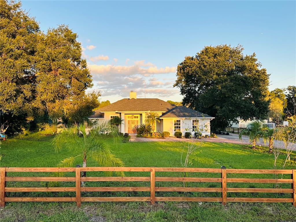 A single-story house with a white exterior and a wooden fence sits on a lawn — 1889 RANCHLAND TRAIL, LONGWOOD, FL