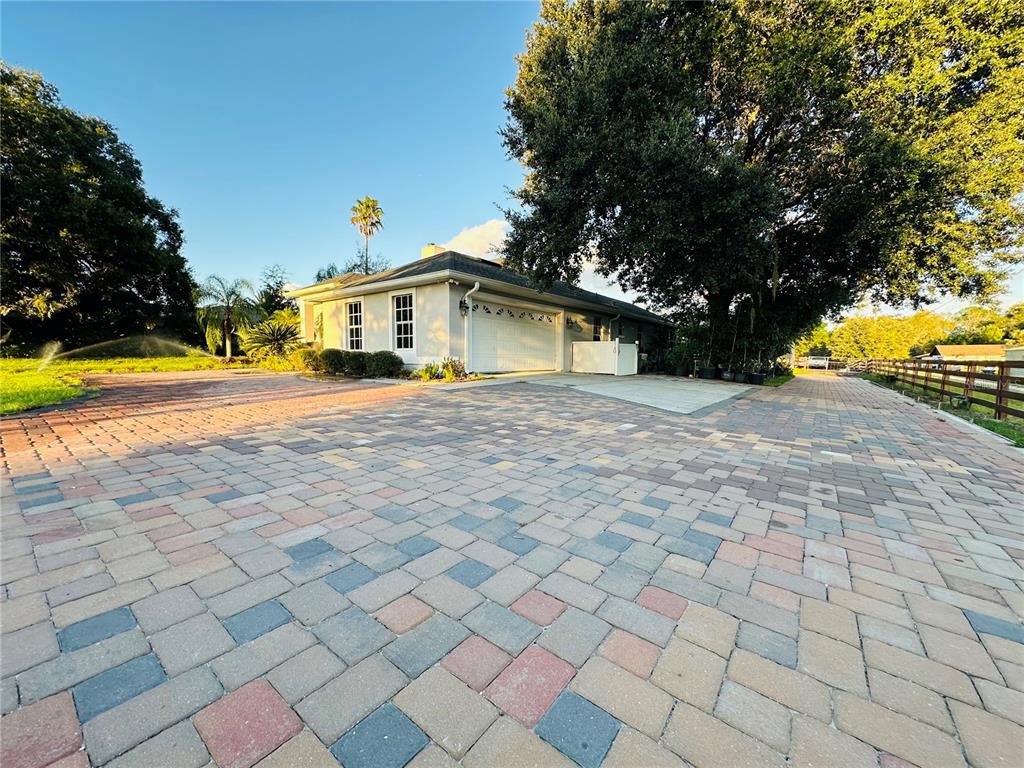 A light-colored house with a multi-colored paver driveway and a large tree in front — 1889 RANCHLAND TRAIL, LONGWOOD, FL