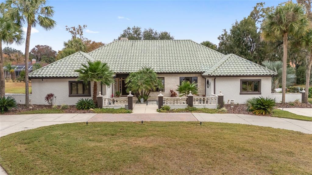 A single-story house with a green tile roof, white stucco walls, and a circular driveway — 2023 SE LAUREL RUN DRIVE, OCALA, FL