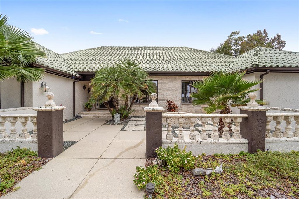 A single-story house with a green tile roof, stone facade, and a gated courtyard entrance — 2023 SE LAUREL RUN DRIVE, OCALA, FL
