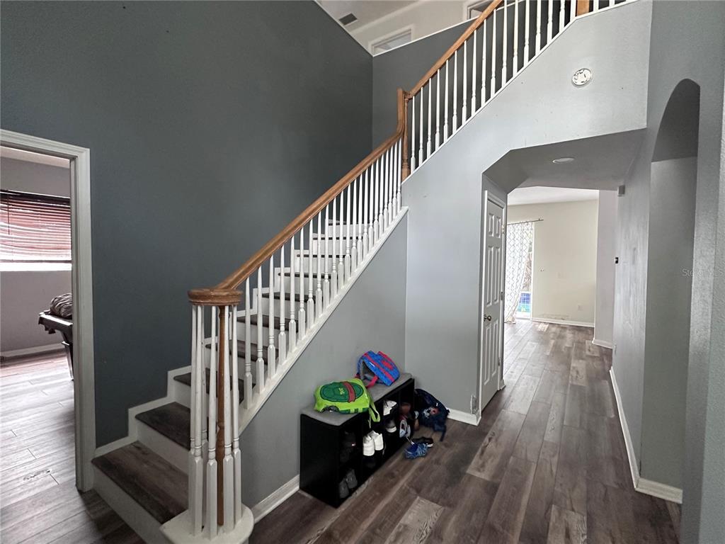 A staircase with a wooden handrail and white spindles sits beside a shoe storage bench — 11116 HOFFNER EDGE DRIVE, RIVERVIEW, FL