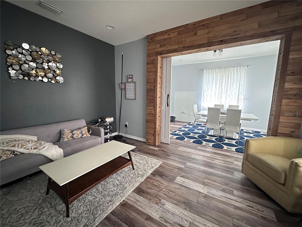 A living room with a gray sofa and wood-paneled doorway leading to a dining area — 11116 HOFFNER EDGE DRIVE, RIVERVIEW, FL