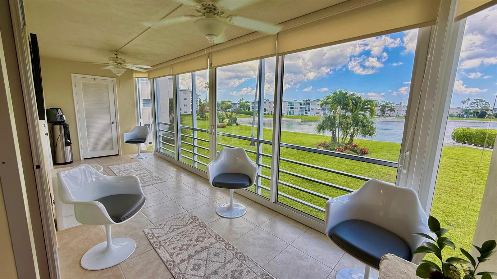 A sunroom features tile flooring, white pedestal chairs, and large windows overlooking a lake — 2728 N Garden Dr Drive N # 214, FL 33461, FL