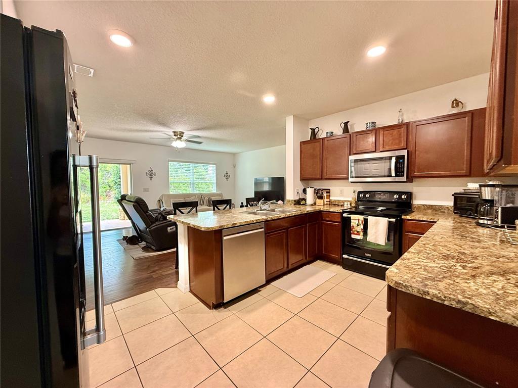 A kitchen with dark wood cabinets, granite countertops, and tile flooring opens to a living area — 331 ALDER AVENUE SE, PALM BAY, FL