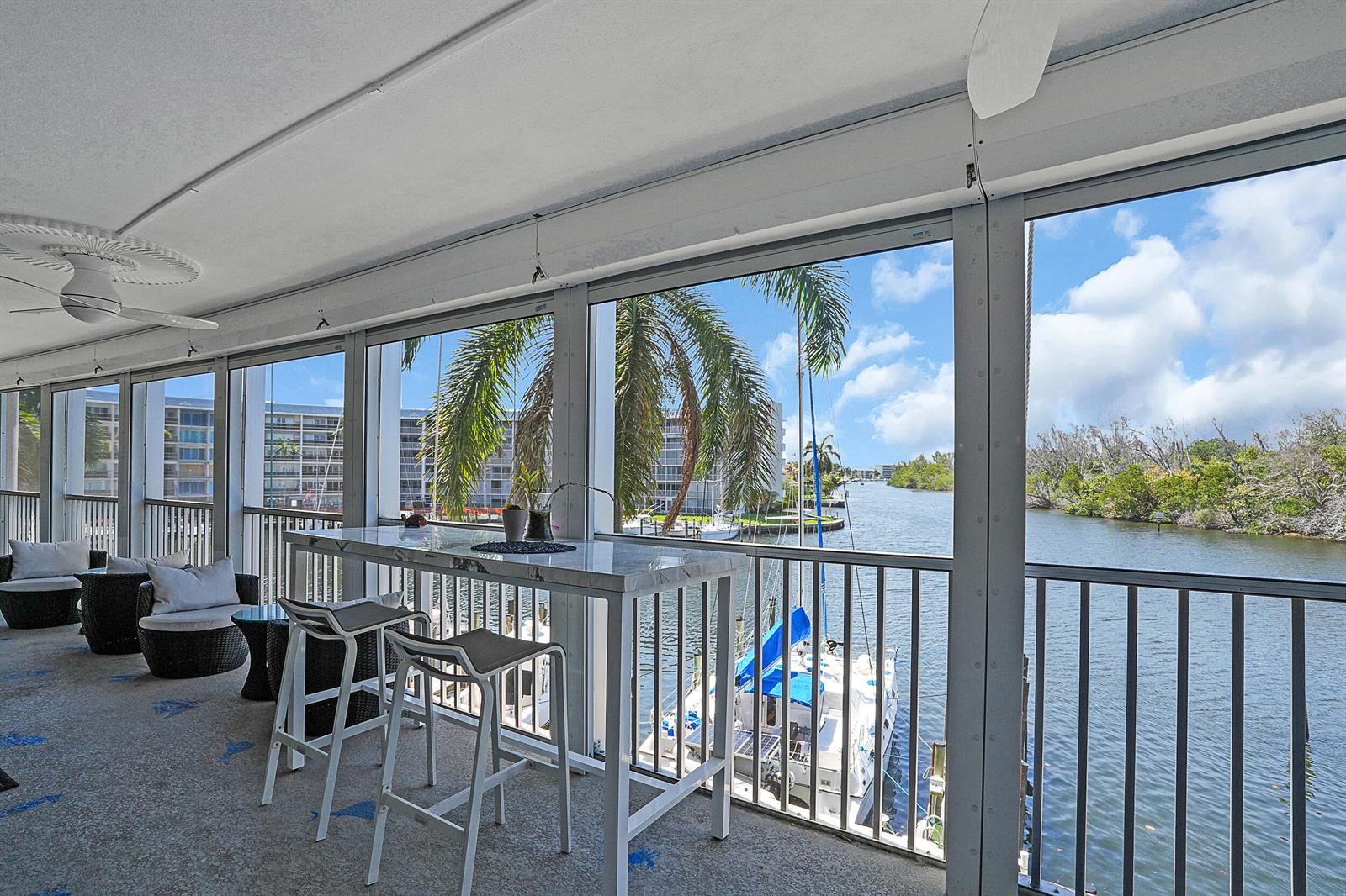 A screened-in balcony features a high-top table, seating, and views of a canal and boats — 1537 E Hillsboro Boulevard # 341, Deerfield Beach FL 33441, DEERFIELD BEACH, FL