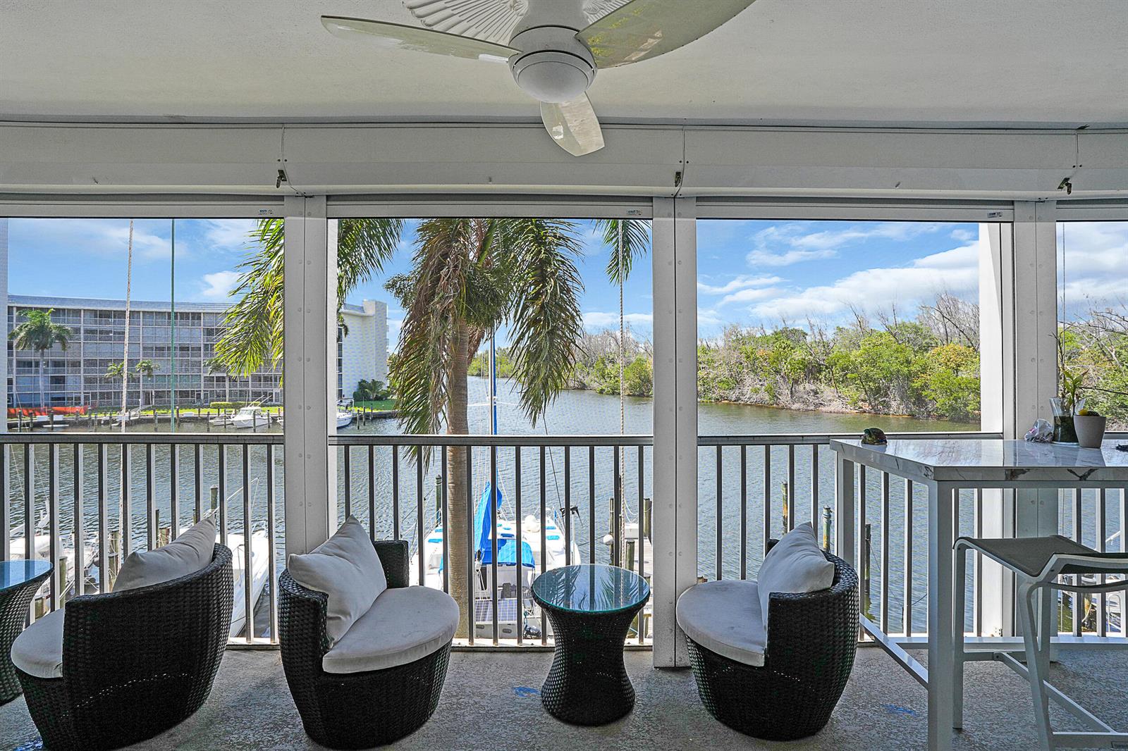 A screened-in balcony features wicker chairs, a small table, and a view of a canal — 1537 E Hillsboro Boulevard # 341, Deerfield Beach FL 33441, DEERFIELD BEACH, FL