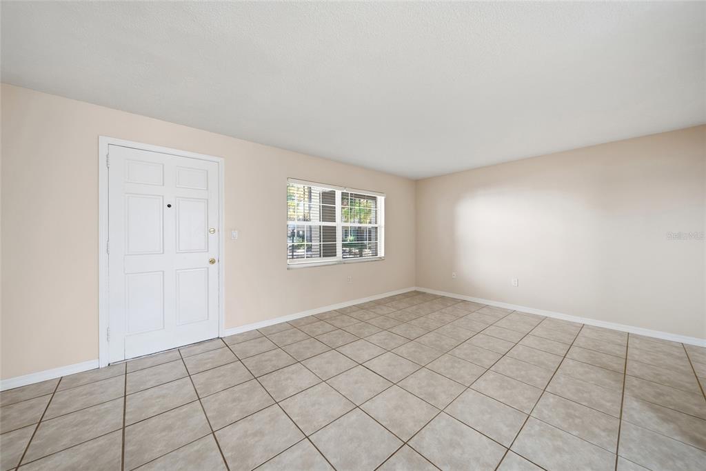 An empty room with beige walls, tile flooring, a white front door, and a window — 4335 AEGEAN DRIVE UNIT 144A, TAMPA, FL