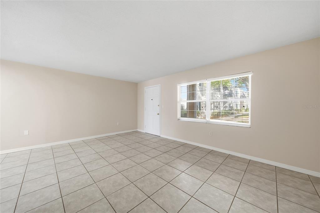 An empty room with beige walls, light-colored tile flooring, a white door, and a window — 4335 AEGEAN DRIVE UNIT 144A, TAMPA, FL
