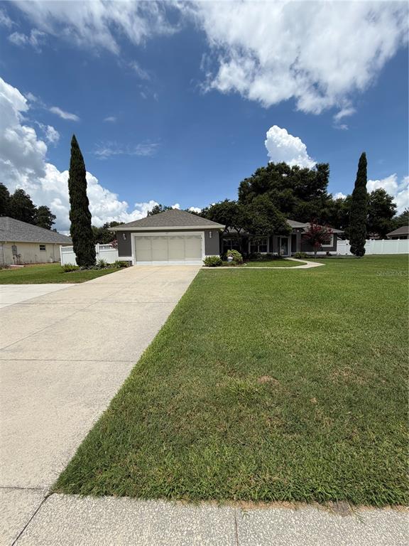 A single-story house with a two-car garage and a large front lawn under a blue sky — 417 ANDERSON DRIVE, TAVARES, FL