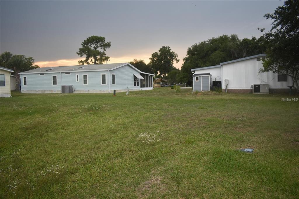 A grassy backyard area between two manufactured homes with a small shed in the distance — LOT 8 BLK C LIBERTY COURT, WILDWOOD, FL