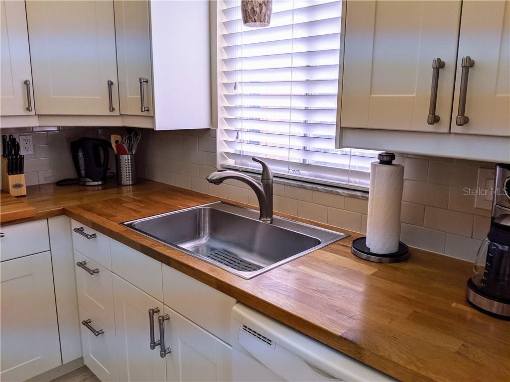A kitchen sink with a wooden countertop and white cabinets sits below a window — 3668 LAKE BAYSHORE DRIVE UNIT K-325, BRADENTON, FL